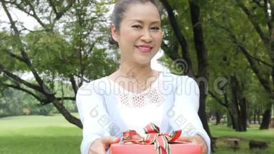 亚洲高级妇女把礼物盒给相机后面的接线员。 女人送礼物。